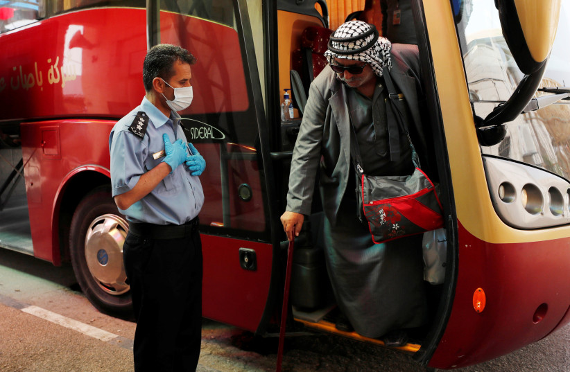  A Palestinian man alights from a bus upon his return from abroad as a police officer wears a mask as a preventive measure against coronavirus, at the Allenby Bridge crossing in Jericho, in the West Bank March 10, 2020. (credit: REUTERS/AMMAR AWAD)