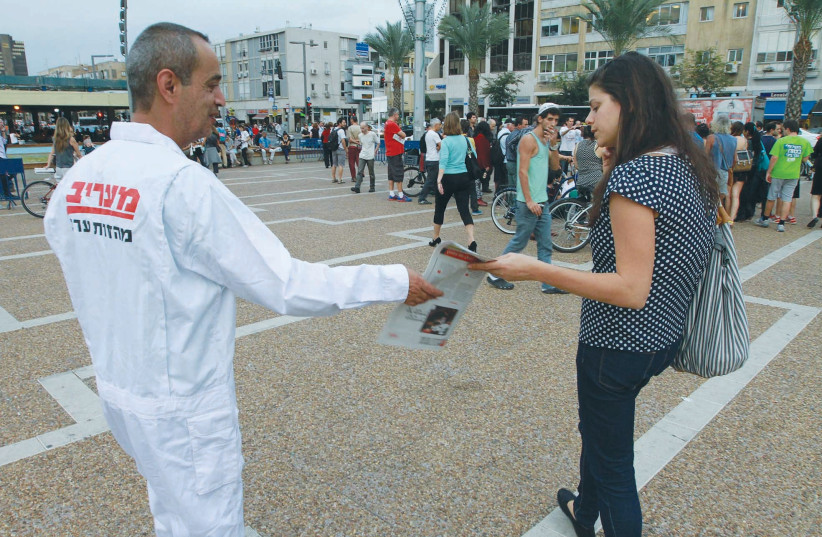  A MAN HANDS out  the ‘Maariv’ newspaper in Tel Aviv’s Rabin Square.   (photo credit: Illustrative file photo: Eli Dassa/Maariv)