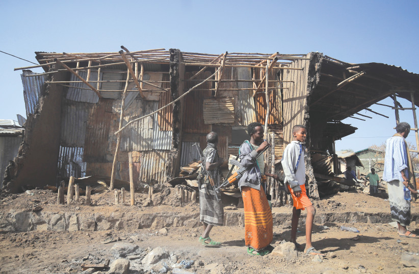 RESIDENTS AND militias stand next to houses destroyed by an air strike during the fight between the Ethiopian National Defense Forces and Tigray People’s Liberation Front in Afar region, Ethiopia, earlier this year.  (photo credit: TIKSA NEGERI / REUTERS)