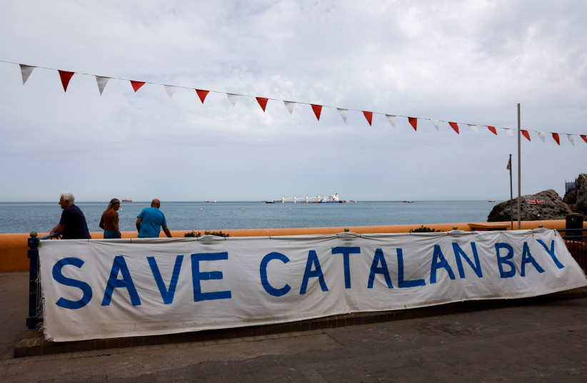  A banner hangs on a fence at a promenade to protest against the construction of a marina while residents look at the cargo ship OS 35, which remains half sunken in Catalan Bay and leaking oil after its collision with an LNG tanker off Gibraltar, September 1, 2022.  (credit: REUTERS/JON NAZCA)