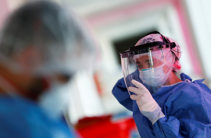  Kinesiologist Maria Luz Porra puts on a mask shield before checking patients suffering from the coronavirus disease (COVID-19) in an intensive care unit of a hospital, on the outskirts of Buenos Aires, Argentina October 16, 2020.  (photo credit: AGUSTIN MARCARIAN/REUTERS)