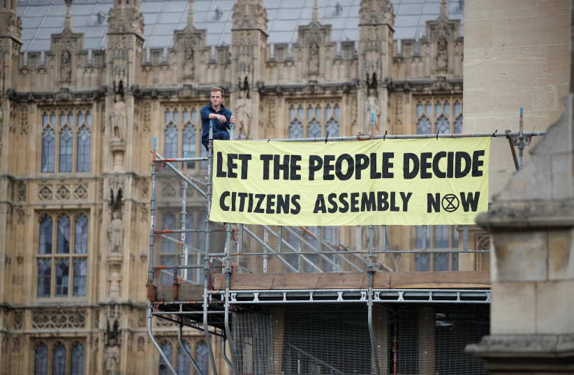  An Extinction Rebellion protester stands with a banner on the scaffolding inside the grounds of the Houses of Parliament in London, Britain September 2, 2022. (credit: REUTERS/PETER NICHOLLS)