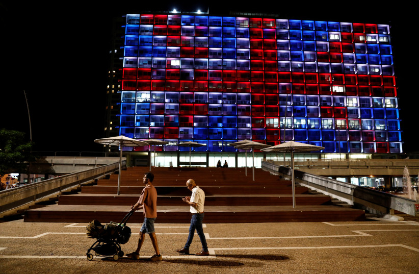  People walk by Rabin square as Tel Aviv's municipality building is illuminated with the Union Jack flag following the death of Queen Elizabeth, Britain's longest-reigning monarch, in Tel Aviv, Israel September 8, 2022. (credit: CORINNA KERN/REUTERS)