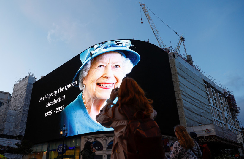  People use their smarthphones as an image of Queen Elizabeth, Britain's longest-reigning monarch and the nation's figurehead for seven decades is displayed at Piccadilly Circus after she died aged 96, according to Buckingham Palace, in London, Britain September 8, 2022. (credit: ANDREW BOYERS/REUTERS)