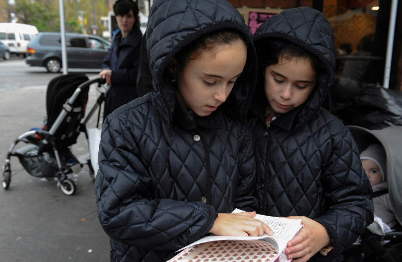  Two girls read the Torah while people participate in the Jewish religious holiday of Kaporos in the Brooklyn borough of New York City, October 9, 2016.  (credit: REUTERS/STEPHANIE KEITH)