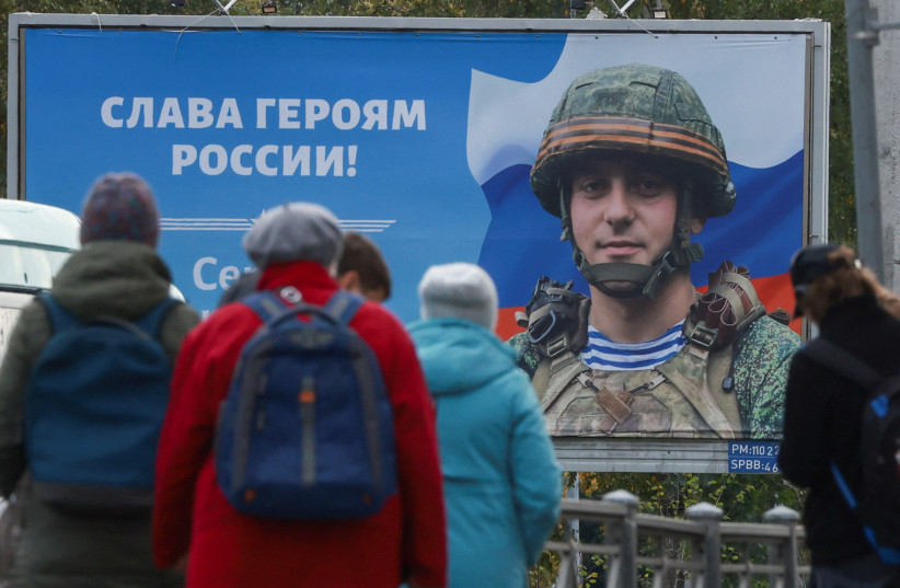  People gather at a tram stop in front of a board displaying a portrait of Russian service member Sergei Tserkovniy in Saint Petersburg, Russia September 21, 2022. A slogan on the board reads: ''Glory to heroes of Russia!'' (credit: REUTERS/ANTON VAGANOV)