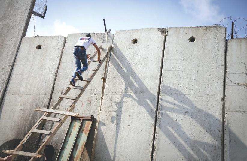  A PALESTINIAN uses a ladder to climb over a section of the separation barrier, near Ramallah in the West Bank. ‘I firmly believe that separation behind barbed wire fences and walls is an anti-peace move,’ says the writer. (photo credit: FLASH90)