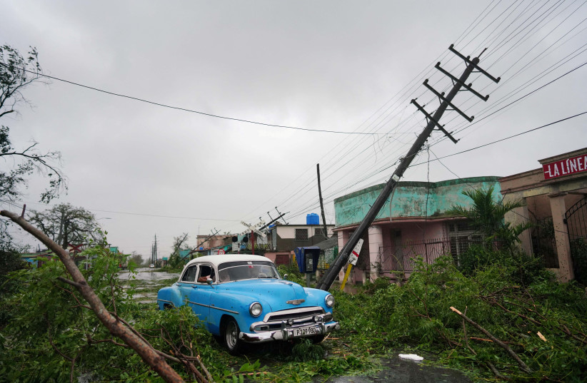  A vintage car passes by debris caused by the Hurricane Ian as it passed in Pinar del Rio, Cuba, September 27, 2022.  (photo credit: ALEXANDRE MENEGHINI/REUTERS)