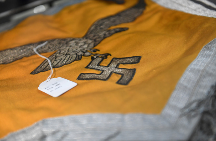  A Nazi flag with an eagle and a swastika is seen in a cupboard at the auction house Hermann Historica in Munich, Germany, November 20, 2019. Several hundred Nazi objects were up for auction, amongst them Adolf Hitler's hat and one of Eva Braun's dresses.  (credit: REUTERS/ANDREAS GEBERT)