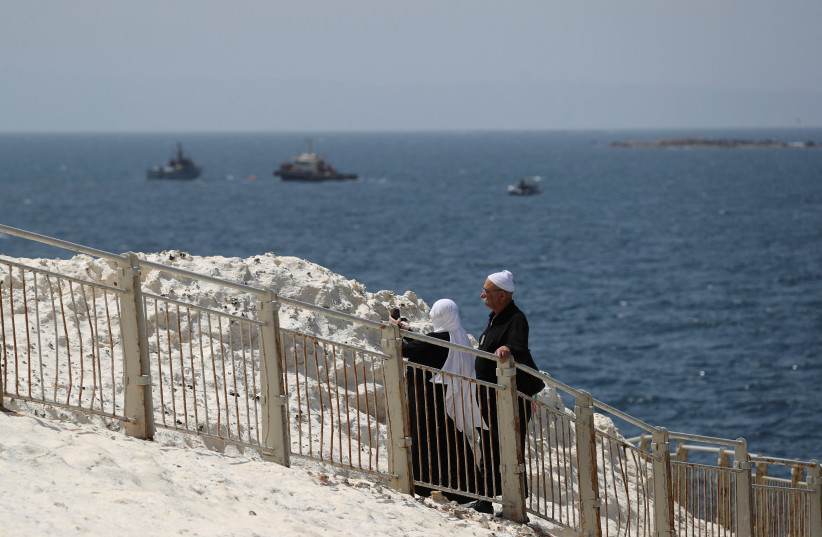  : People walk as Israeli navy boats are seen in the Mediterranean Sea as seen from Rosh Hanikra, close to the Lebanese border, northern Israel May 4, 2021.  (photo credit: REUTERS/AMMAR AWAD)