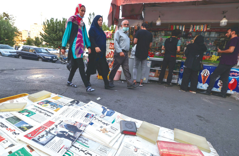  IRANIANS WALK past a newspaper stall with a paper’s front page bearing a title reading in Farsi ‘The night of the end of the JCPOA,’ in Tehran last August.  (photo credit: Atta Kenare/AFP via Getty Images)
