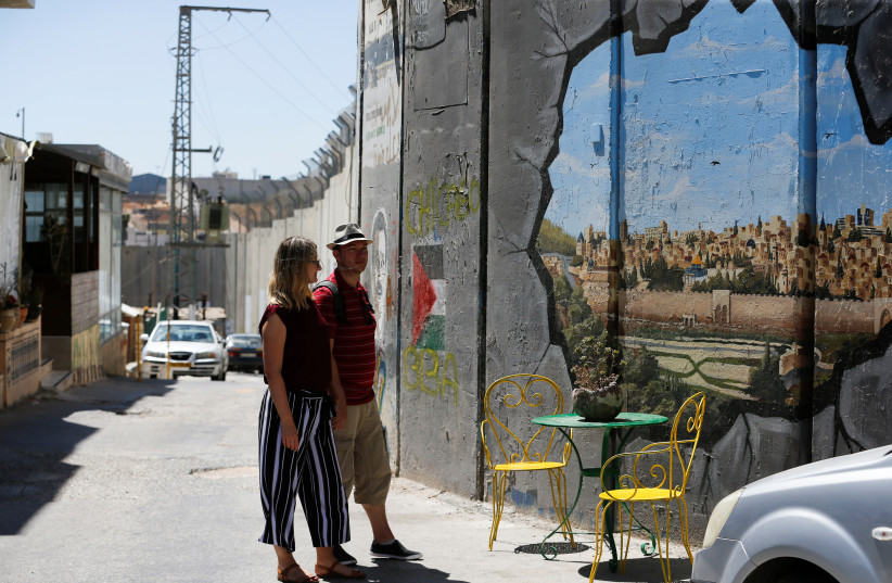  German tourists look at a mural on the Israeli barrier in Bethlehem, in the West Bank June 20, 2022. (credit: REUTERS/MUSSA QAWASMA)