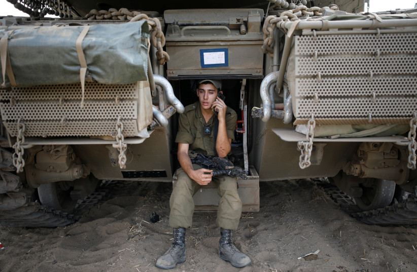  An Israeli soldier speaks on a phone as he sits on a tank positioned with other military armoured vehicles in an open area near Israel's border with the Gaza Strip October 18, 2018. (photo credit: AMIR COHEN/REUTERS)