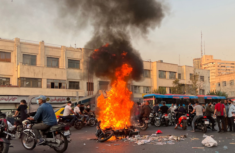 People gathering next to a burning motorcycle in the capital Tehran on October 8, 2022. - Iran has been torn by the biggest wave of social unrest in almost three years, which has seen protesters, including university students and even young schoolgirls chant "Woman, Life, Freedom". (photo credit: AFP VIA GETTY IMAGES)
