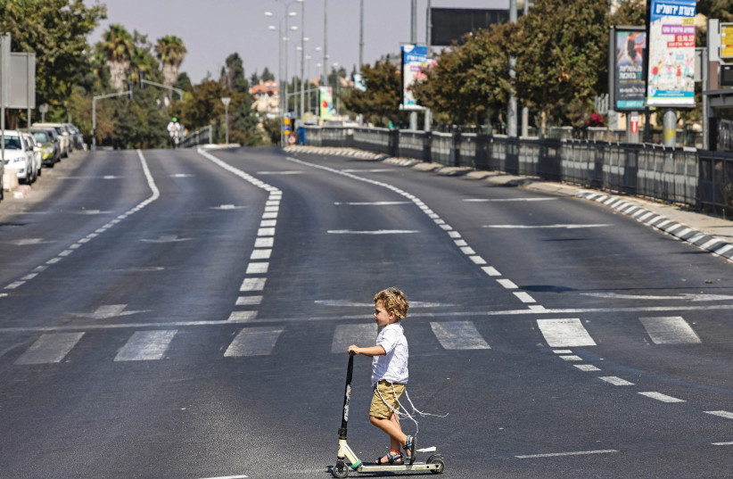  A CHILD RIDES his scooter in an empty avenue in Jerusalem on Yom Kippur, last month.  (photo credit: Ronaldo Schemidt/AFP via Getty Images)