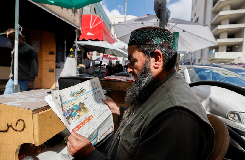  A Palestinian vendor reads news about Israeli elections in a newspaper, in Hebron in the West Bank November 2, 2022. (photo credit: MUSSA QAWASMA/REUTERS)