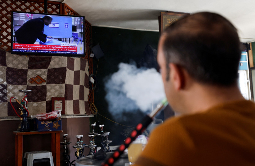  A Palestinian smokes shisha as he watches TV news about the Israeli elections, in Hebron in the West Bank, November 1, 2022. (credit: MUSSA QAWASMA/REUTERS)