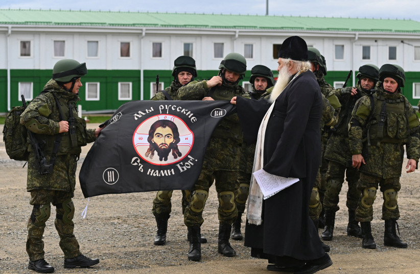 A priest conducts a ceremony for Russian reservists recruited during the partial mobilisation of troops before their departure to the zone of Russia-Ukraine conflict, in the Rostov region, Russia October 31, 2022. The sign on the flag reads " We are Russians. God is with us!" (photo credit: SERGEY PIVOVAROV/REUTERS)