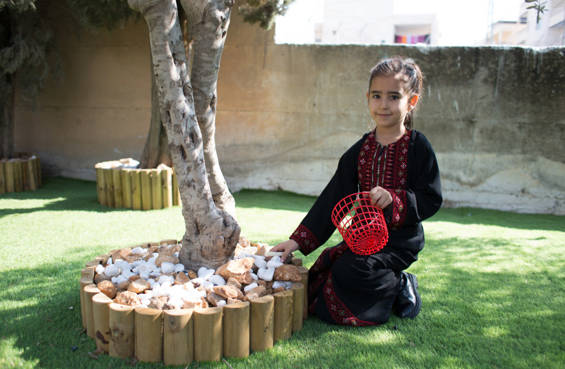  A young girl places stones at the base of a tree in the new garden at Beit Anan Girls School in the West Bank during the garden's inaugural ceremony on November 10, 2022.  (photo credit: LOUISE WATERIDGE/UNRWA)