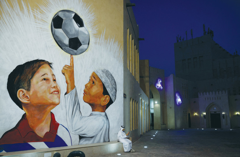  A MAN sits beside a football mural on the walls of Katara Cultural Village ahead of the World Cup in Qatar.  (photo credit: JOHN SIBLEY/REUTERS)