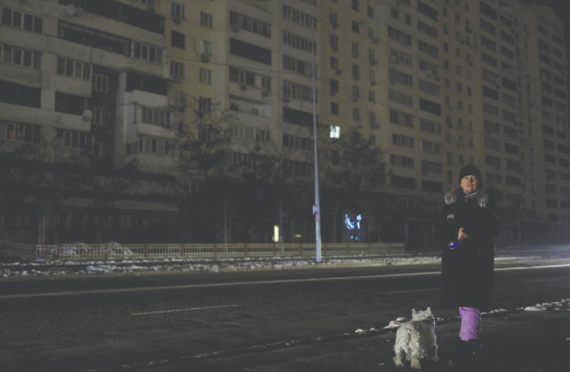  A WOMAN walks with her dog on a Kyiv street without electricity after civil infrastructure was hit in Russian missile attacks last week.  (photo credit: VALENTYN OGIRENKO/REUTERS)