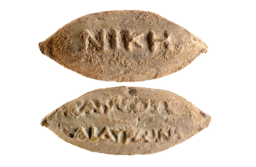  The word "Victory" on one side of the sling bullet, and the names of the gods Heracles and Hauronas on the reverse side. (photo credit: DAFNA GAZIT/ISRAEL ANTIQUITIES AUTHORITY)