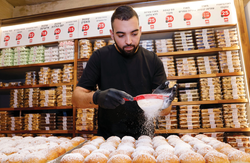 A man pours powdered sugar onto Hanukkah jelly donuts (sufganiyot) at the Marzipan bakery in Jerusalem's Mahaneh Yehuda shuk. (credit: MARC ISRAEL SELLEM/THE JERUSALEM POST)
