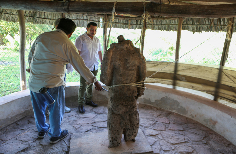  Workers of Mexico's National Institute of Anthropology and History (INAH) talk next to a sculpture carved in stone representing the Mayan god of fertility Yum Kee, in the archaeological zone of Oxkintok, in Maxcanu, state of Yucatan, in Mexico, December 7, 2022.  (photo credit: REUTERS/Lorenzo Hernandez)