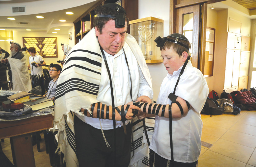  A FATHER teaches his son how to wear tefillin.  (photo credit: GERSHON ELINSON/FLASH90)