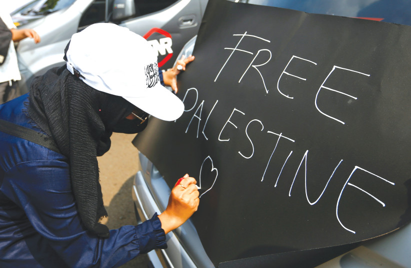  A PROTESTER writes a placard reading ‘Free Palestine,’ during a protest against Israel outside the US Embassy in Jakarta, last year. When people shout ‘Free Palestine,’ it is a call for genocide, another Holocaust, says the writer. (photo credit: AJENG DINAR ULFIANA/REUTERS)