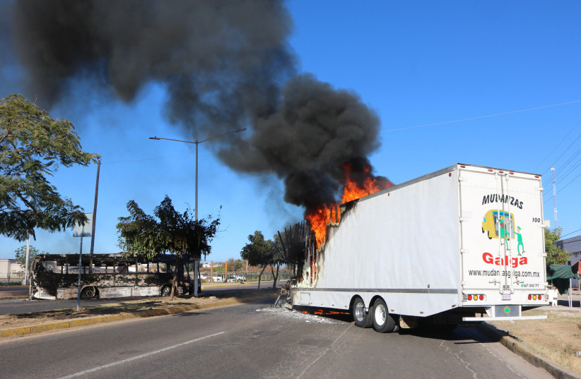 The wreckage of a bus and a burning truck, set on fire by members of a drug gang are pictured following the detention of Mexican drug gang leader Ovidio Guzman, a son of incarcerated kingpin Joaquin "El Chapo" Guzman, who has been arrested by Mexican authorities, in Culiacan, Mexico, Jan. 5, 2023.  (photo credit: STRINGER/ REUTERS)