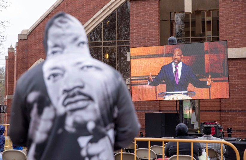  US Senator, Reverend Raphael Warnock is displayed on a screen as people gather outside of Ebenezer Baptist Church to view a commemorative service to mark Martin Luther King Jr Day in Atlanta, Georgia, US, January 17, 2022. (photo credit: REUTERS/ALYSSA POINTER)