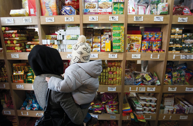  A woman carrying her son stands in front of a food shelf as she shops at a supermarket in northern Tehran. (credit: Morteza Nikoubazl/Reuters)