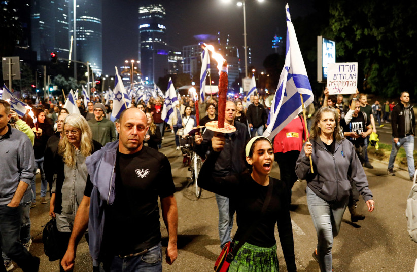 A protester holds a torch during a demonstration against proposed judicial reforms by Israel's new right-wing government in Tel Aviv, Israel, January 28, 2023. (photo credit: REUTERS/CORINNA KERN/FILE PHOTO)