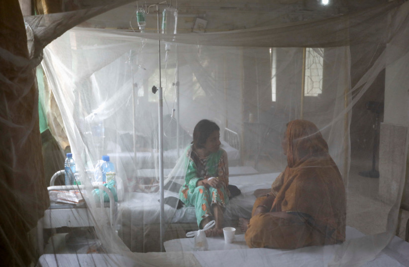 A patient suffering from dengue fever chats with a woman while sitting under a mosquito net inside a dengue and malaria ward at the Sindh Government Services Hospital in Karachi, Pakistan, September 21, 2022. (credit: REUTERS/AKHTAR SOOMRO)