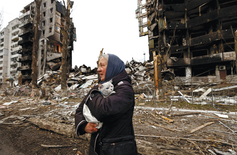  A woman carries her cat as she walks past buildings destroyed by Russian shelling in Borodyanka, April 5, 2022.  (credit: ZOHRA BENSEMRA/REUTERS)