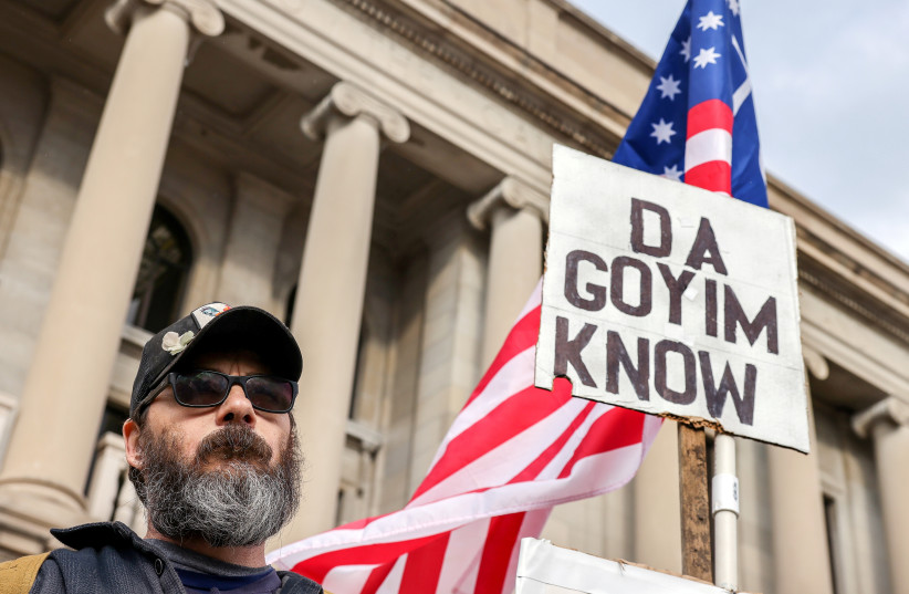 A protester carries a white supremacist and antisemitic sign outside the Kenosha County Courthouse on the second day of jury deliberations in the Kyle Rittenhouse trial, in Kenosha, Wisconsin, US, November 17, 2021. (credit: REUTERS/EVELYN HOCKSTEIN)