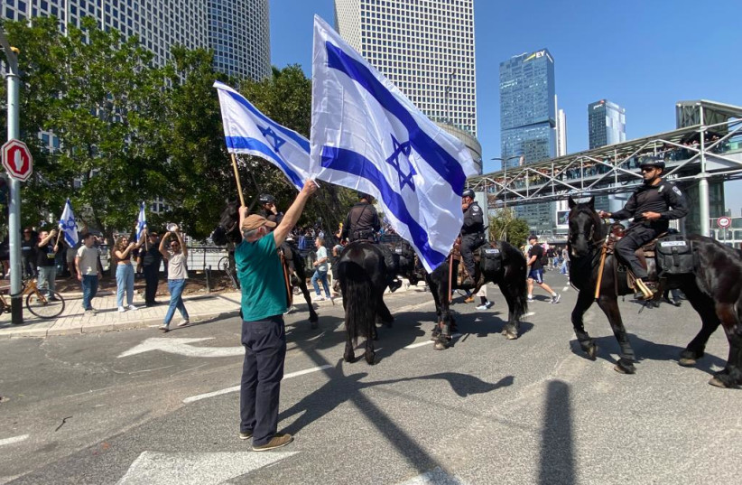  A protester stands facing the police waving Israeli flags on Ayalon Highway during a protest against judicial reform, March 1, 2023. (photo credit: AVSHALOM SASSONI/MAARIV)