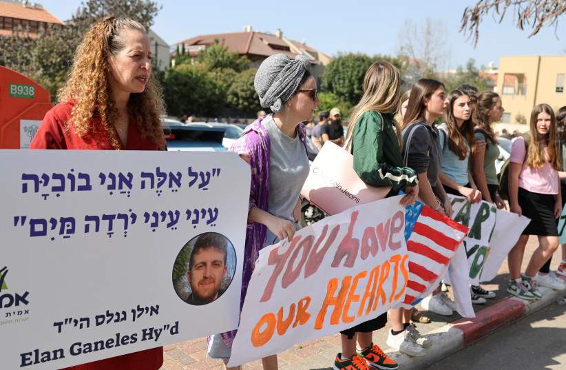 Les gens tiennent des pancartes alors qu'ils pleurent Elan Ganeles, un double citoyen américano-israélien tué dans une fusillade alors qu'il conduisait près de la ville cisjordanienne de Jéricho par un tireur palestinien présumé, lors de ses funérailles, à l'extérieur du cimetière, à Raanana, Israël, 1er mars 2023 (crédit photo : REUTERS)
