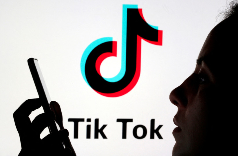  A person holds a smartphone as Tik Tok logo is displayed behind in this picture illustration taken November 7, 2019. (photo credit: REUTERS/DADO RUVIC/ILLUSTRATION)