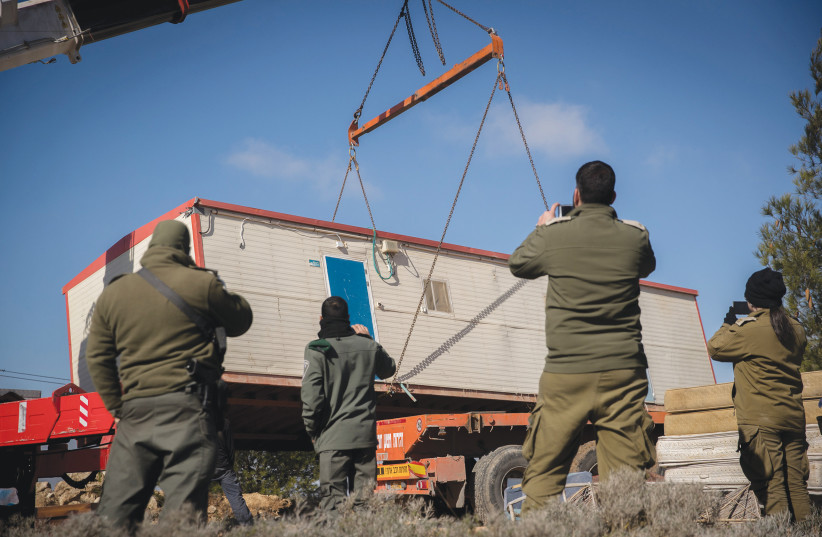  SECURITY FORCES watch as a prefab home is removed at the settler outpost of Amona, in 2019.  (photo credit: YONATAN SINDEL/FLASH90)