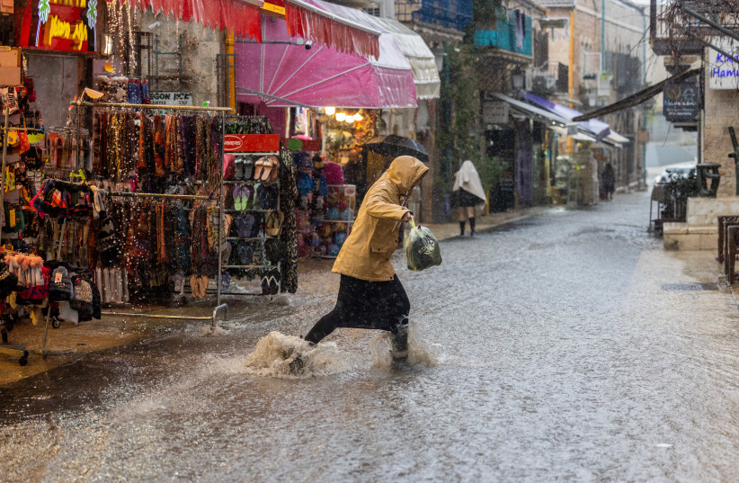 A woman walks in a flooded street during heavy rain in downtown Jerusalem, on March 14, 2023. (credit: YONATAN SINDEL/FLASH90)