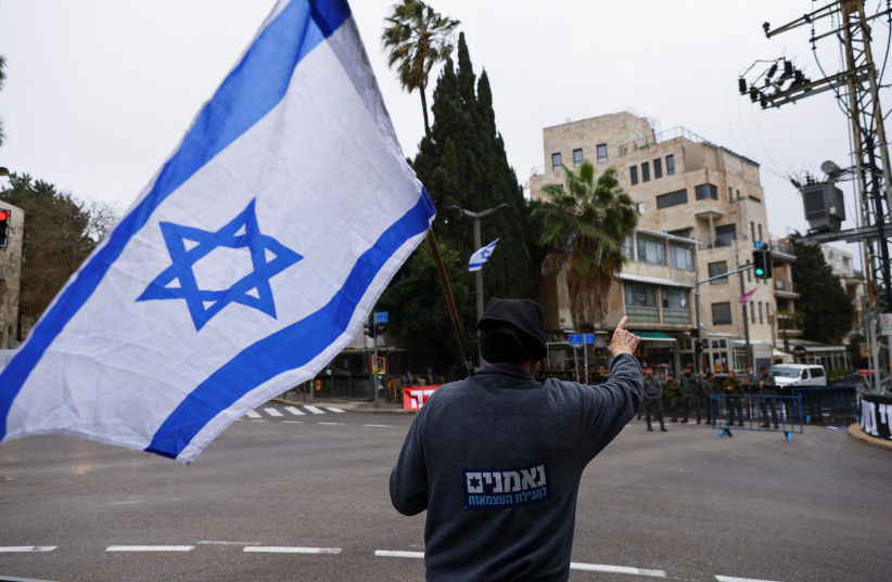  A person holding an Israeli flag gestures during a judicial reform protest near the private residence of Israeli Prime Minister Benjamin Netanyahu in an attempt to disrupt his departure to Berlin for a state visit (photo credit: REUTERS)
