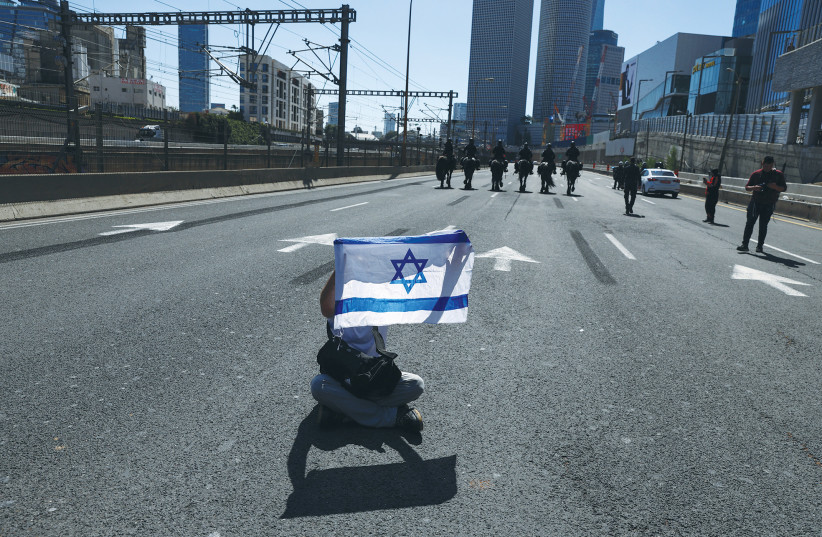  A LONE protester sits on the ground as mounted police officers patrol the street in Tel Aviv yesterday, the day after the coalition rejected President Isaac Herzog’s plan to resolve the crisis over the government’s judicial overhaul plans. (photo credit: RONEN ZVULUN/REUTERS)