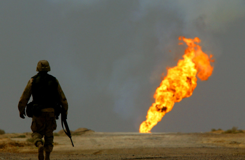 A US Army soldier walks towards a burning oil well in Iraq's vast southern Rumaila oilfields, March 30, 2003. (credit: REUTERS/YANNIS BEHRAKIS/FILE PHOTO)