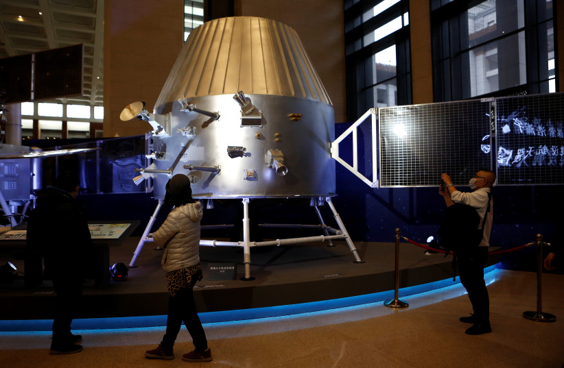 Visitors stand near a replica of a lunar orbiter from China's lunar exploration program Chang'e-5 Mission during an exhibition inside the National Museum in Beijing, China, March 3, 2021. (credit: REUTERS/TINGSHU WANG)