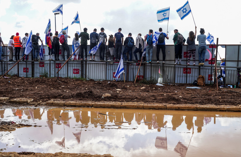  Protesters stand on a fence during a demonstration after Israeli Prime Minister Benjamin Netanyahu dismissed the defense minister and his nationalist coalition government presses on with its judicial overhaul, in Jerusalem, March 27, 2023. (credit: REUTERS/ITAI RON)