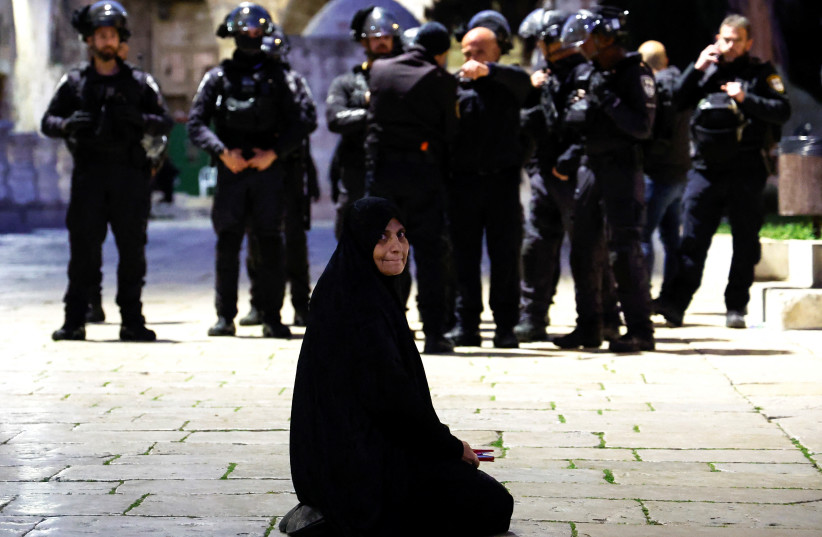  A Palestinian woman sits near Israeli border policemen in the Al-Aqsa compound, also known to Jews as the Temple Mount, while tension arises during clashes with Palestinians in Jerusalem's Old City, April 5, 2023. (credit: AMMAR AWAD/REUTERS)