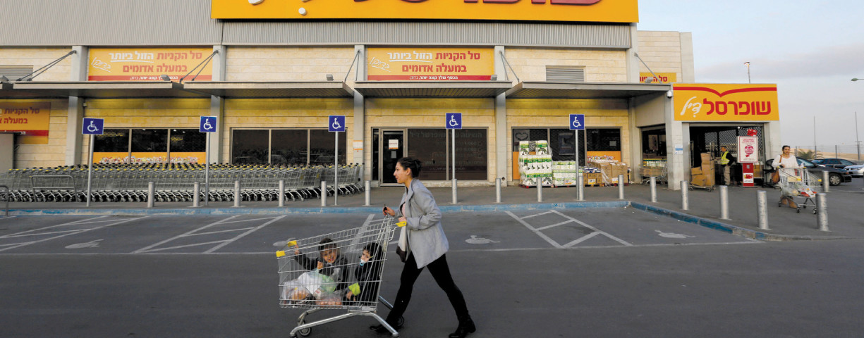 A WOMAN pushes children in a shopping cart in front of a Shufersal ‘Sheli’ in Ma’aleh Adumim