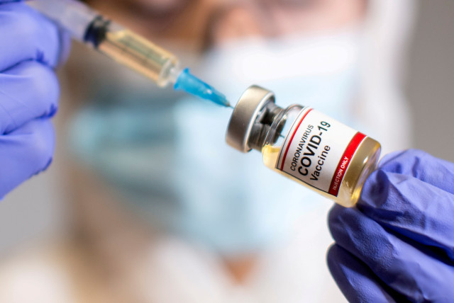 A woman holds a small bottle labeled with a "Coronavirus COVID-19 Vaccine" sticker and a medical syringe, October 30, 2020. (photo credit: REUTERS/DADO RUVIC/FILE PHOTO)
